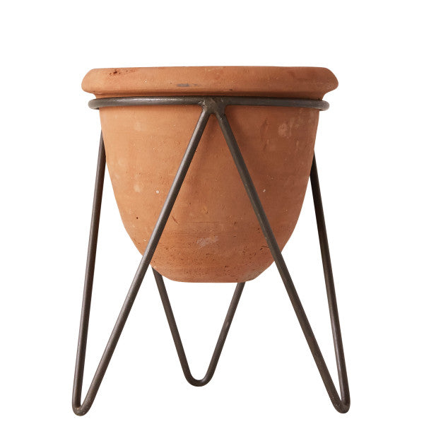 A terracotta pot with metal stand, viewed from a slight angle, displaying the pot's brown color and the metallic legs supporting it.